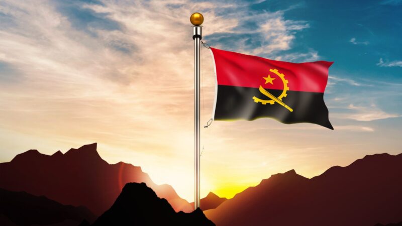 The flag of Angola on a big pole with sunrise behind it