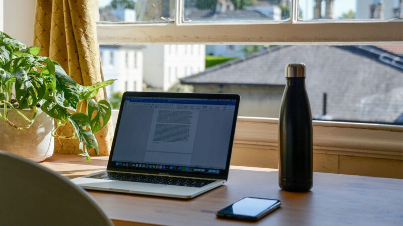 Laptop on a wooden table next to water bottle